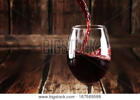 Closeup of glass with red wine on wooden background. Close up of pouring wine into transparent glass. Perfect alcoholic background. Macro of red wine in tall glass.