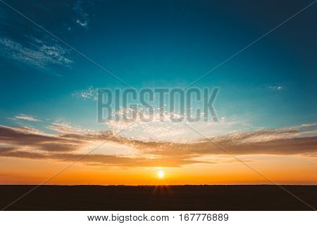 Natural Sunset Sunrise Over Field Or Meadow. Bright Dramatic Sky And Dark Ground. Countryside Landscape Under Scenic Colorful Sky At Sunset Dawn Sunrise. Sun Over Skyline, Horizon. Warm Colours.