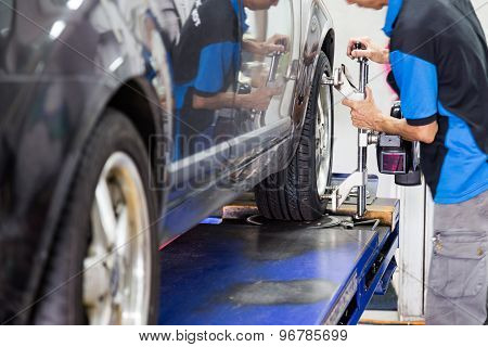 Mechanic fixing the wheel alignment device onto a car wheel. Focus is on the car wheel and wheel ali