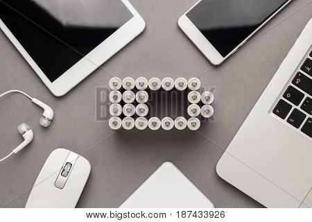 conceptual image of battery charge level pictogram made of rechargeable batteries with some mobile devices that use battery accumulators like smart phone, tablet computer, laptop and power bank. battery concept over grey background