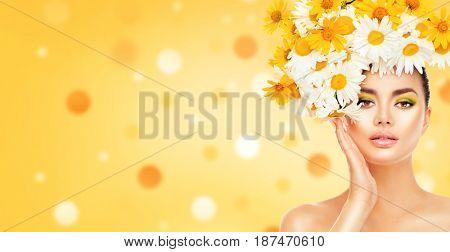 Beauty Girl with Daisy Flowers Hair Style touching her face skin. Beautiful Model woman with Blooming chamomile flowers on her head. Nature Hairstyle. Summer. Holiday Creative Makeup. Fashion Make up