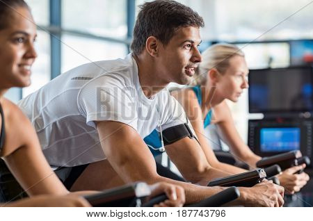 Portrait of young man exercising using stationery bike in gym. Latin man biking in the gym with a group of people. Fitness class doing sport biking in the gym for fitness.