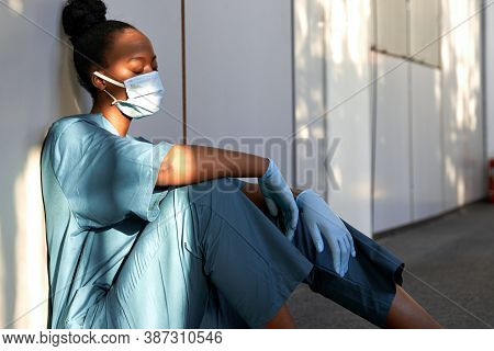 Tired Exhausted Female African Scrub Nurse Wears Face Mask Blue Uniform Gloves Sits On Hospital Floo