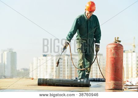 Roofer installing Roofing felt with heating and melting of bitumen roll by torch on flame during roof repair