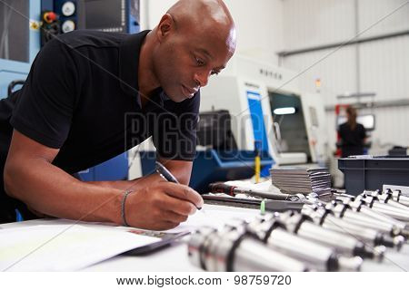 Engineer Planning Project With CNC Machinery In Background