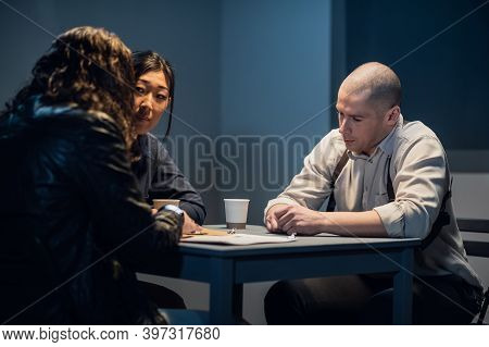 In The Interrogation Room, The Investigator And The Officer Are Talking To The Criminal.