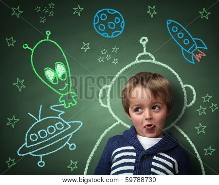 Imagination and dreams of a child, dressed as a space man in front of a blackboard with chalk drawings of space rocket and alien, concept for aspirations and daydreaming