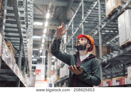 Warehouse manager checking his inventory in a large warehouse. using the tablet via the Internet is checking stock availability