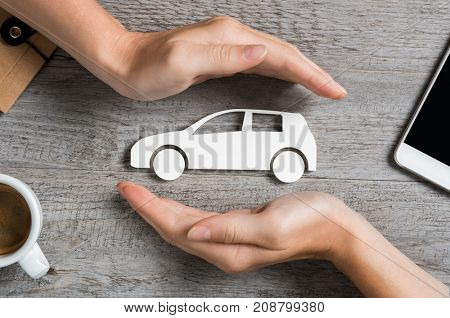 Hands protecting icon of car over wooden table. Top view of hands showing gesture of protecting car. Car insurance and automotive business concept.