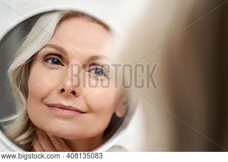 Happy 50s Middle Aged Woman Model Touching Face Skin Looking In Mirror Reflection. Smiling Mature Ol