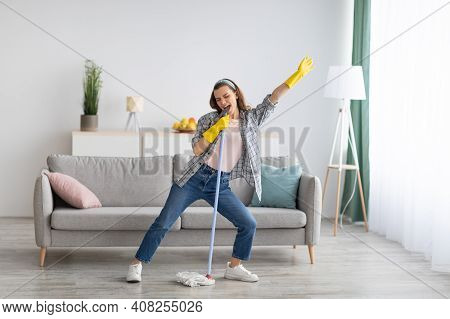 Happy Young Woman Cleaning Her Home, Singing At Mop Like At Microphone And Having Fun, Free Space. M