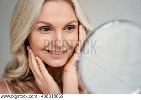 Happy 50s Middle Aged Woman Model Touching Face Skin Looking In Mirror. Smiling Mature Older Lady Pa