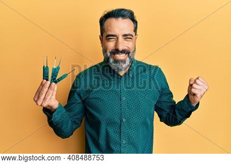 Middle age man with beard and grey hair holding picklock to unlock security door screaming proud, celebrating victory and success very excited with raised arm 