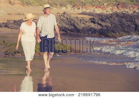 lovely senior mature couple on their 60s or 70s retired walking happy and relaxed on beach sea shore in romantic aging together and retirement husband and wife lifestyle concept