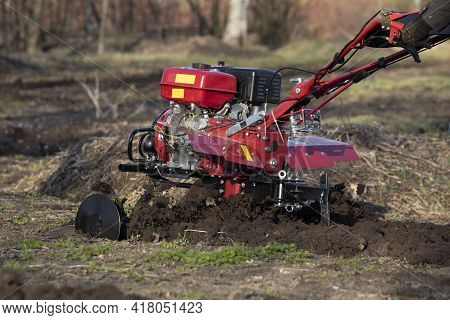 A Farmer Man Plows The Land With A Cultivator. Machinery Cultivator For Soil Cultivation In The Gard