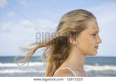 Caucasian pre-teen girl on beach with hair blowing in wind.