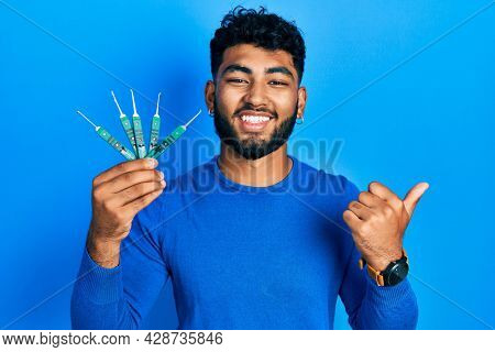 Arab man with beard holding picklock to unlock security door pointing thumb up to the side smiling happy with open mouth 