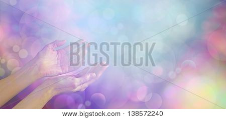 Supernatural Phenomenon - female healing hands gently cupped up facing towards an ethereal blue white light orb on a muted multicolored bokeh background with plenty of copy space