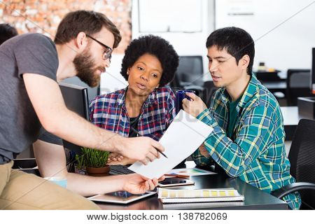 Man holding paper showing colleagues business people office diverse mix race group businesspeople working sitting desk looking document casual wear