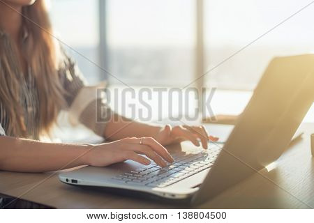 Female writer typing using laptop keyboard at her workplace in the morning. Woman writing blogs online, side view close-up picture