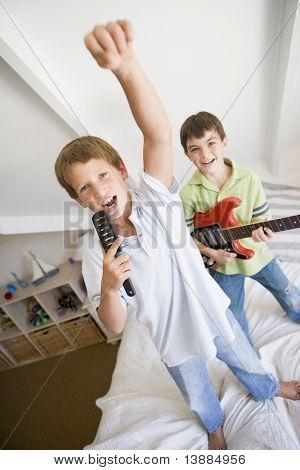 Two Boys Standing On A Bed, Playing Guitar And Singing Into A Hairbrush