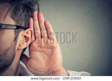 Man Holds His Hand Near Ear And Listens Carefully Isolated On Gray Wall Background