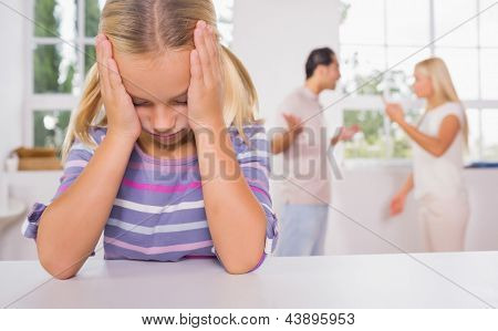 Little girl looking depressed in front of fighting parents in the kitchen