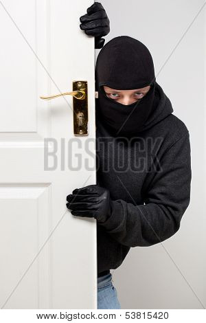 Home burglary concept with a burglar sneaking in a open house door