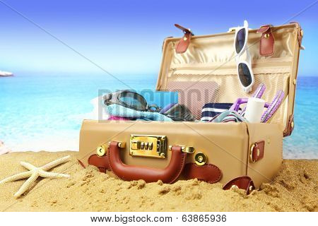 Full open suitcase on tropical beach background 