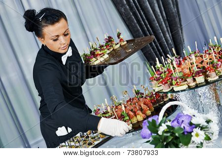 Waiter with meat dish serving catering table with food snacks during party event