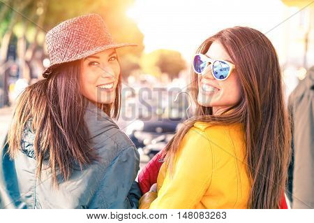 Young women walking on the street turning back and smiling - Cheerful girlfriends carefree attitude looking at camera outdoors with day light and car background - Concept of friendship and leisure