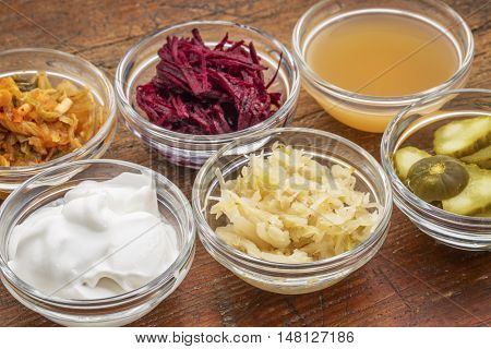 a sampler of fermented food great for gut health - glass bowls against wood:  kimchi, red beets, apple cider vinegar, coconut milk yogurt, cucumber pickles, sauerkraut