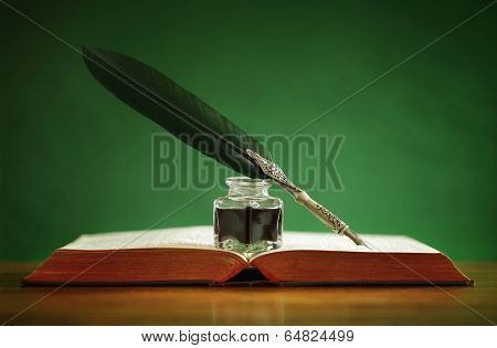 Quill pen and inkwell resting on an old book with green background concept for literature, writing, author and history