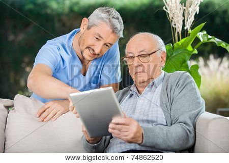 Male caretaker assisting senior man in using digital tablet at nursing home porch