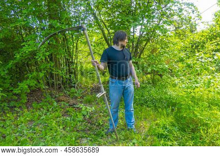 A Man Mows The Grass With A Hand Scythe. Mow The Grass With An Old Scythe. The Farmer Traditionally 