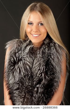 Happy beautiful woman in fur clothing, isolated over dark background