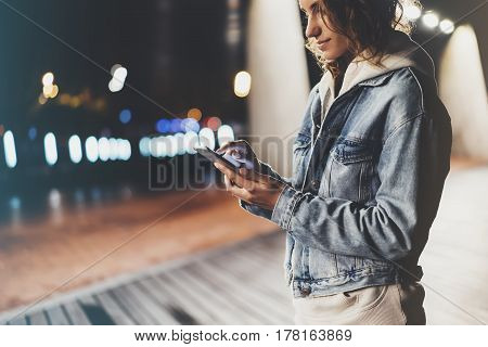 Girl pointing finger on screen smartphone on background illumination bokeh color light in night atmospheric city hipster using in female hands and texting mobile phone mockup glitter street content lifestyle