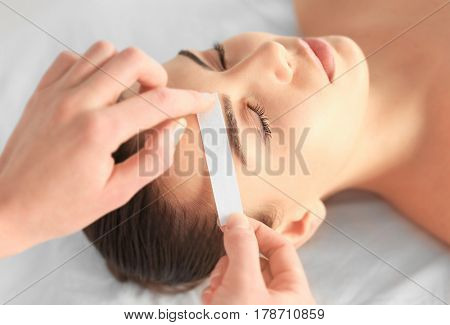 Beautician waxing young woman's eyebrows in spa center