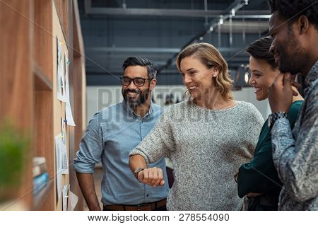 Group of mature businesspeople planning business strategy while looking at infographic on wall. Business men and casual women looking at pie charts. Successful startup partners feeling happy.