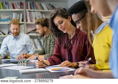 Businesswoman training young business man while explaining graph. African businessman analyzing report with team. Group of multiethnic creative business people sitting while working at financial plan.