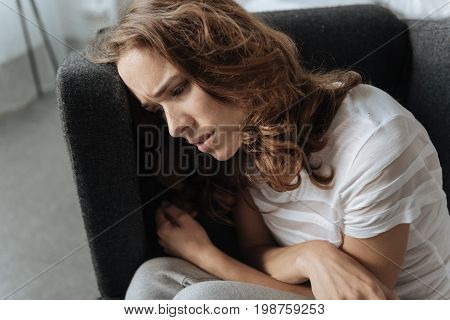 Period of depression. Unhappy depressed moody woman leaning on the armchair and suffering from depression while having a bad time in her life