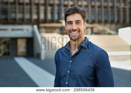 Portrait of happy young man in casual clothing looking at camera outdoor. Smiling man with beard feeling confident. Successful business man in city street.