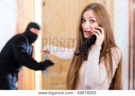 Security - disguised burglar breaking in an apartment or office, a woman calling the police with her phone or telephone