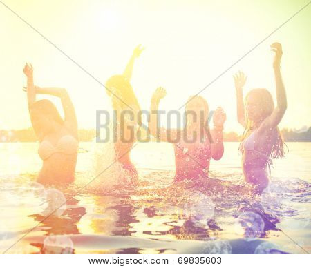 Group of happy teen girls playing in water at the beach on sunset. Beauty and joyful teenager friends having fun, dancing and spraying over summer sunset. Beach party. Sun flare.