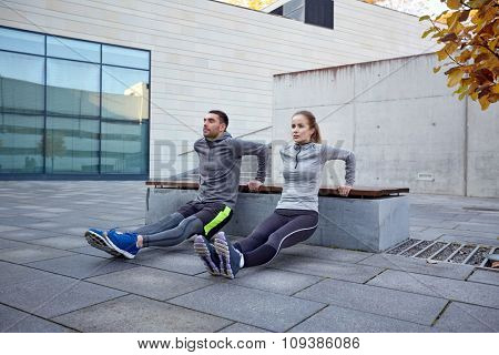 fitness, sport, training, people and lifestyle concept - couple doing triceps dip exercise on bench outdoors