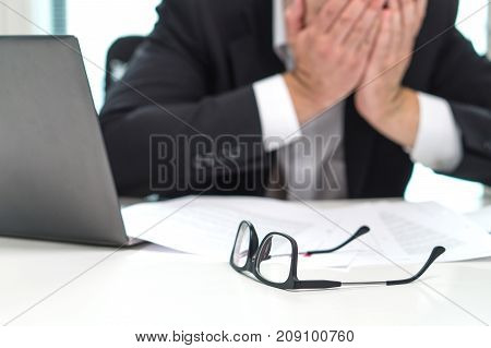 Stressed business man covering face with hands in office. Working over time or too much. Problem with failing business or confusion with crisis. Entrepreneur in bankruptcy. Burnout and overwork.