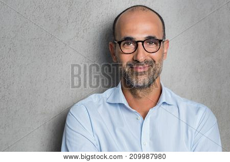 Portrait of a mature businessman wearing glasses on grey background. Happy senior latin man looking at camera isolated over grey wall with copy space. Close up face of happy successful business man.