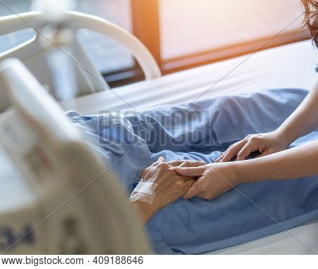 Caregiver And Elderly Senior Patient (aged Old Adult Person) Holding Hands In Hospital Bed Or Nursin