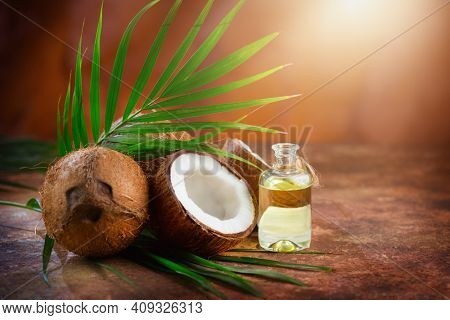 Coconut palm oil in a bottle with coconuts and green palm tree leaf on brown background. Coco nut closeup. Healthy Food, skin care concept. Vegan food. Skincare treatments. Aromatherapy.