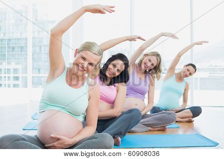 Pregnant women in yoga class sitting on mats stretching arms in a fitness studio